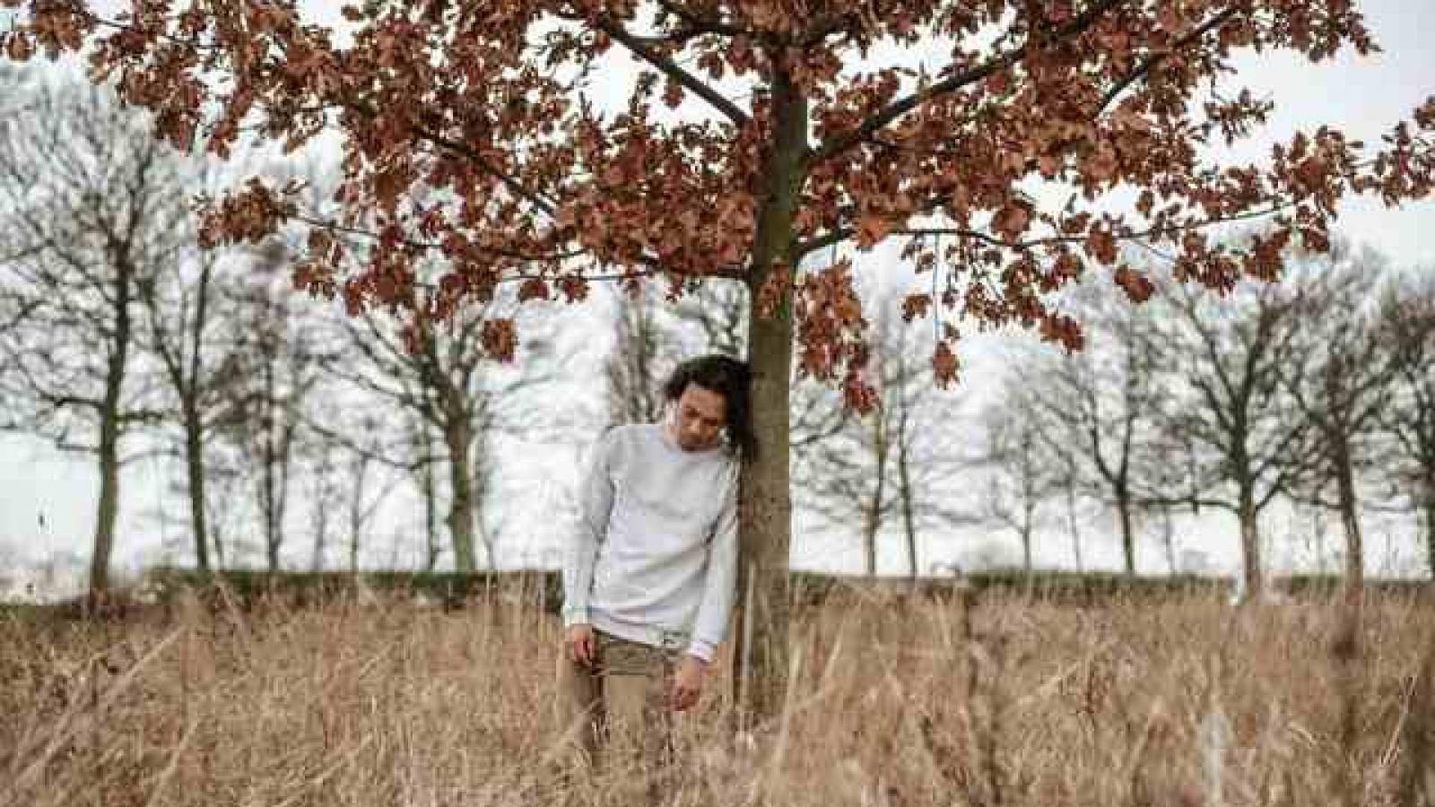 A man leans sadly against a tree