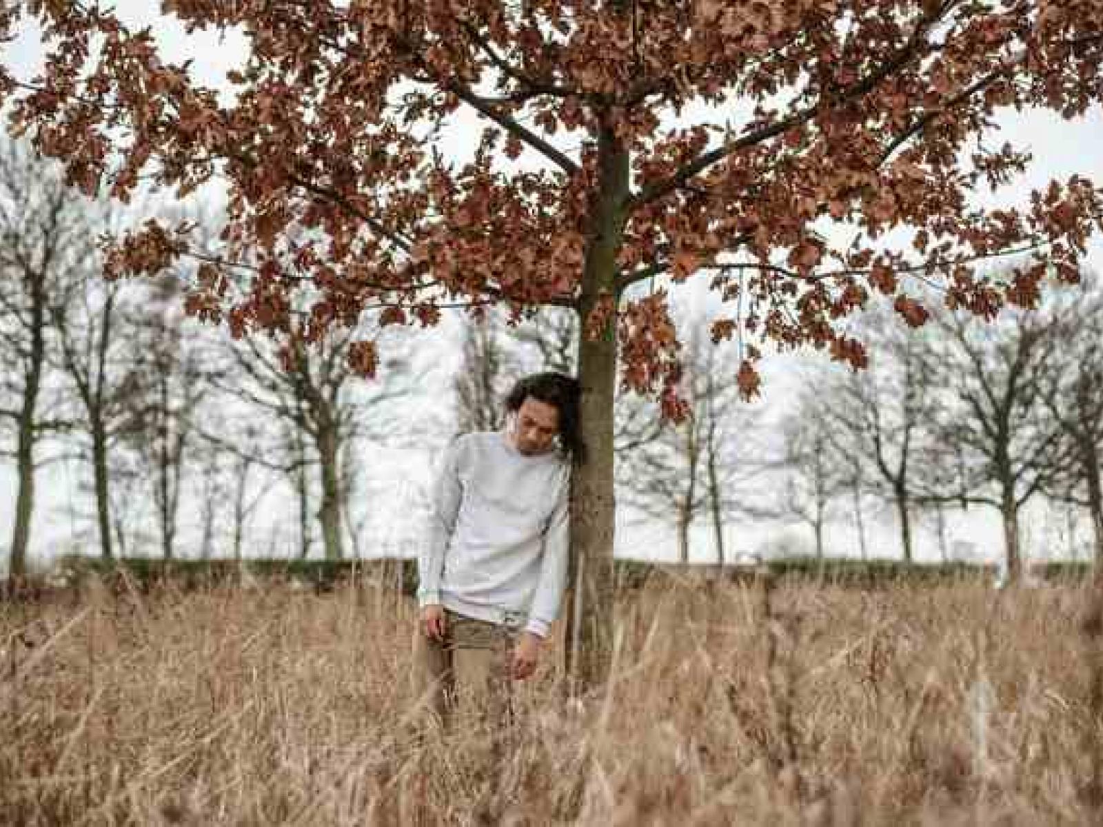 A man leans sadly against a tree
